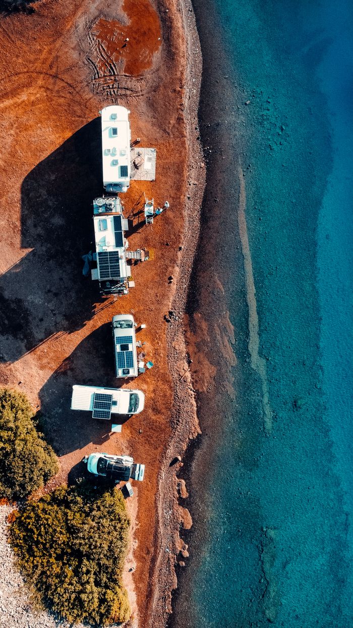 Overhead view of parked campers lined on the Marmaris shore, overlooking the clear turquoise sea.